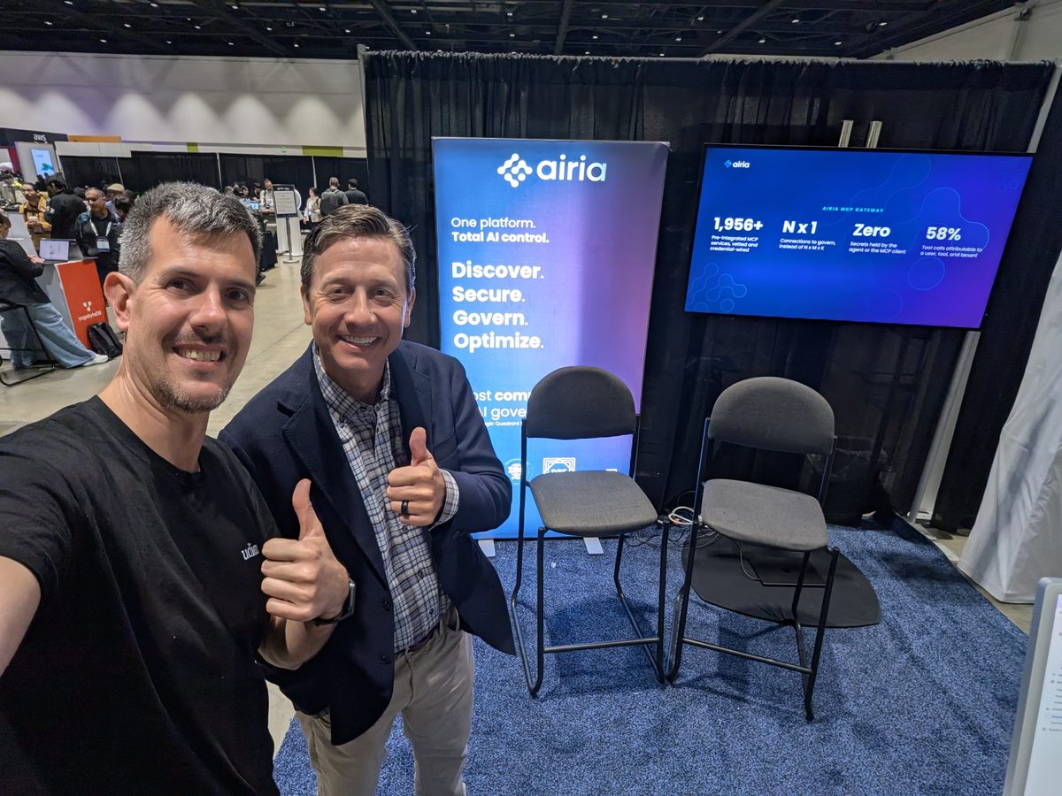 Luca Berton and Spencer Reagan giving a thumbs-up at the Airia booth, screens with Airia figures behind them