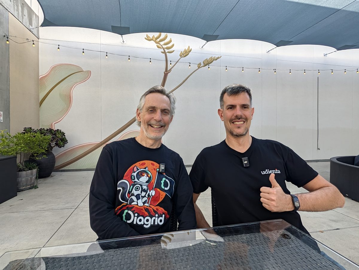 Mark Fussell, in a black Diagrid sweatshirt, and Luca Berton giving a thumbs-up at a table in the convention center