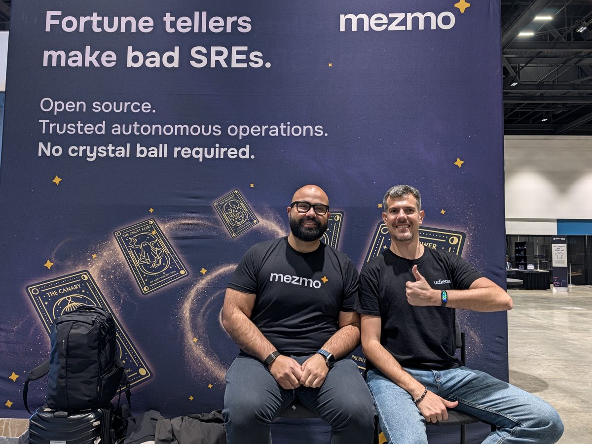 Andre Elizondo and Luca Berton sitting in front of the Mezmo booth wall that reads Fortune tellers make bad SREs. Open source. Trusted autonomous operations. No crystal ball required.
