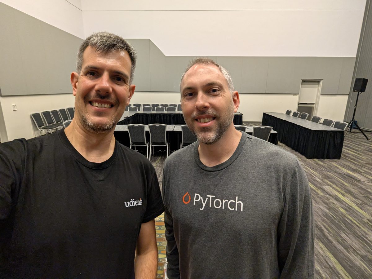 Luca Berton in an Udienza T-shirt and Jonathan Bryce in a grey PyTorch shirt, smiling, in a meeting room of the convention center