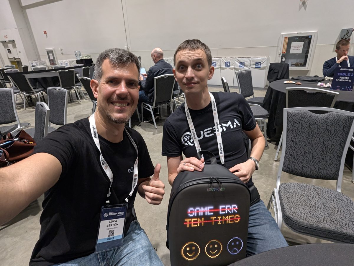 Luca Berton and Jacek Migdał at the Quesma booth, a black backpack with an LED screen reading GAME ERR TEN TIMES in front of them