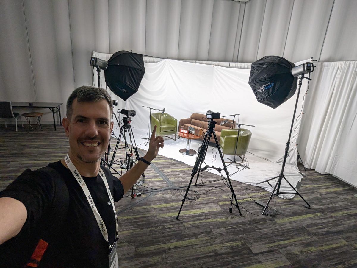 Luca Berton in the conference podcast studio: a white backdrop, two armchairs, softbox lights and cameras on tripods