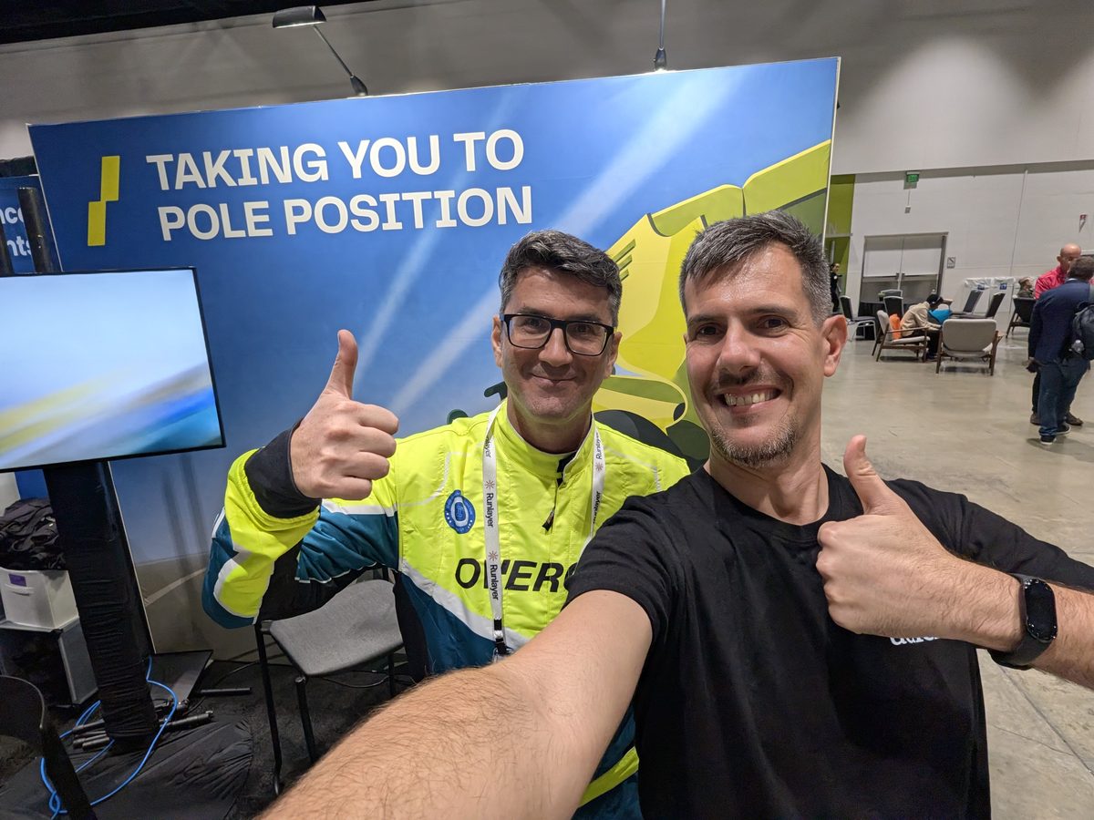 Luca Berton and Yuval Hazaz, in a racing suit, giving a thumbs-up at the Overcut booth under a banner reading Taking you to pole position