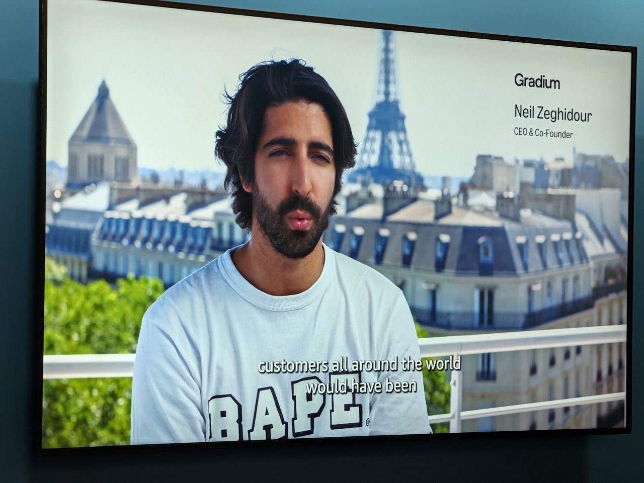 A stand screen playing a video interview with Neil Zeghidour, CEO and co-founder of Gradium
