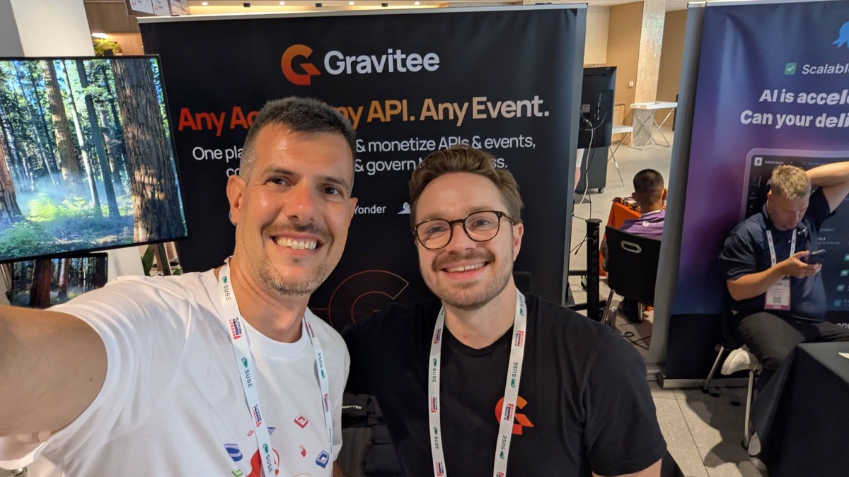 The host at the Gravitee stand at PlatformCon London, with a Gravitee representative in front of the Any API, Any Event backdrop