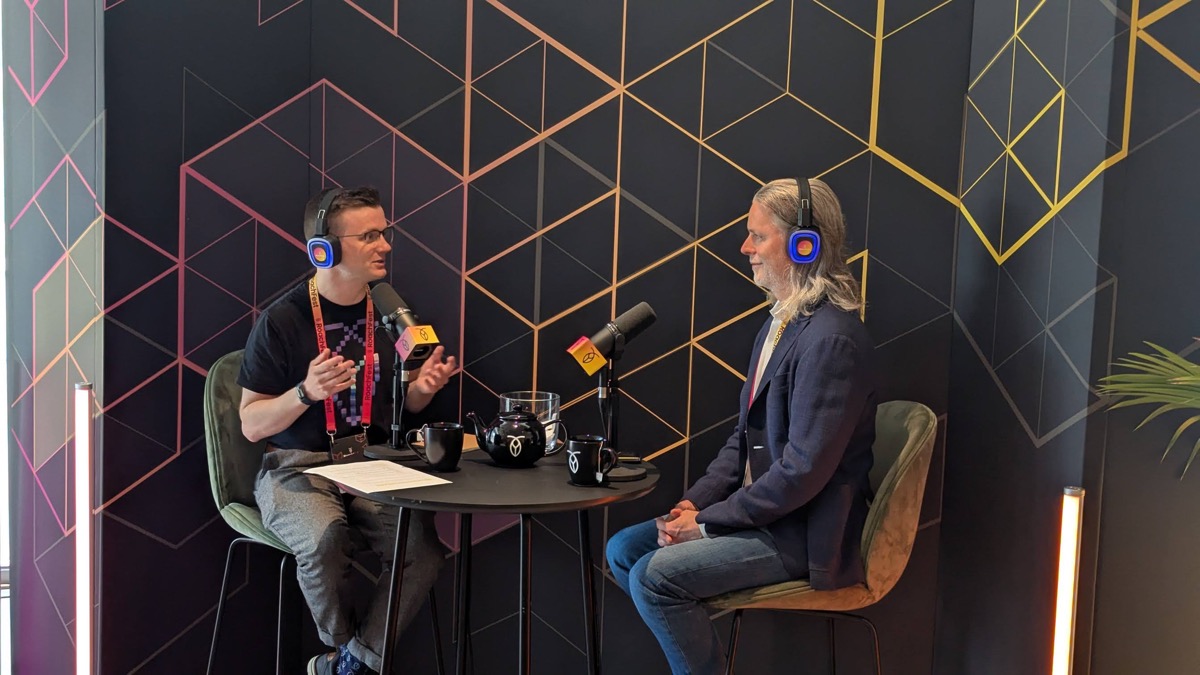 Two people recording a podcast at a branded set on the RoachFest floor, seated with headphones and microphones
